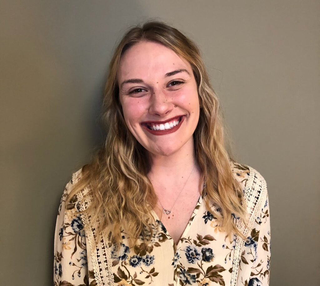 A woman smiling for the camera in front of a wall.